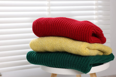 Stack of woolen sweaters on table near window, closeup