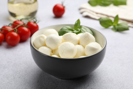 Tasty mozzarella cheese balls, tomatoes and basil on light grey table, closeupの写真素材
