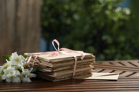 Stack of love letters and flowers on wooden table. Space for text