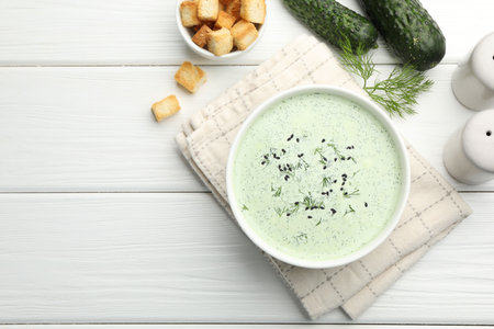 Tasty cucumber soup, croutons and ingredients on white wooden table, flat lay. Space for textの写真素材
