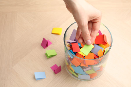 Woman taking paper with message out of jar at wooden table, closeup. Space for text