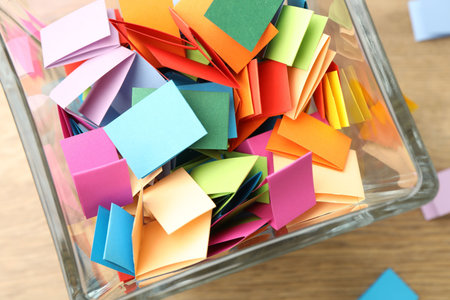 Jar with colorful pieces of paper on wooden table, top viewの写真素材