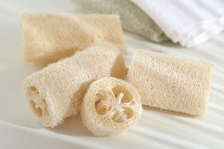 Different loofah sponges and towels on white table, closeup