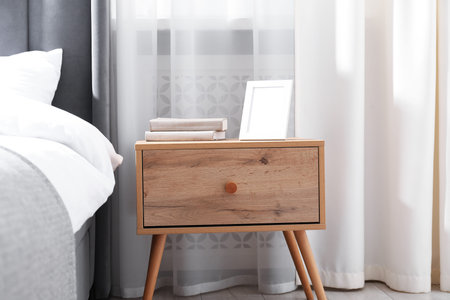 Bedside table with books and frame near bed indoors