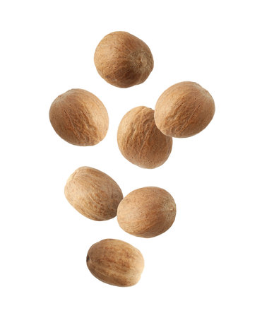 Aromatic nutmeg seeds falling on white background