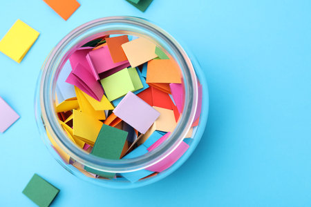 Jar with colorful pieces of paper on light blue background, flat layの写真素材