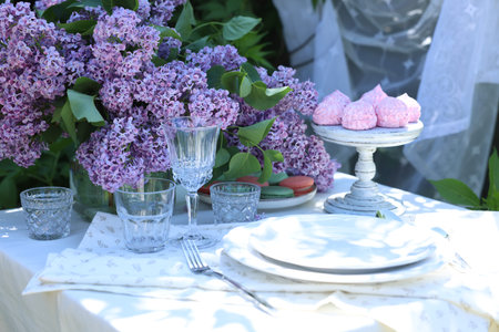 Beautiful lilac flowers, sweets, plates, cutlery and glasses on table in gardenの写真素材