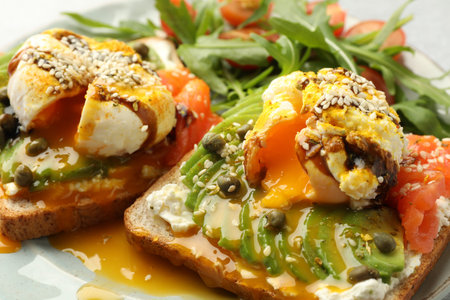 Delicious sandwiches with avocado, poached egg and salmon on table, closeup