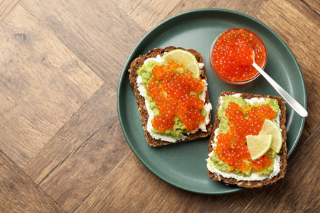 Delicious sandwiches with avocado, red caviar, cream cheese and lime on wooden table, top view. Space for textの写真素材