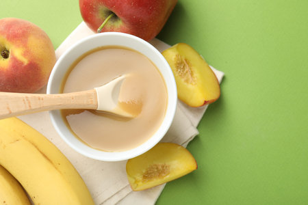 Baby food. Tasty puree in bowl and ingredients on green background, flat lay. Space for textの写真素材