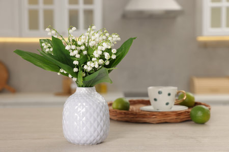 Beautiful lily-of-the-valley in vase, limes and cup of tea on wooden table in kitchen, closeupの写真素材