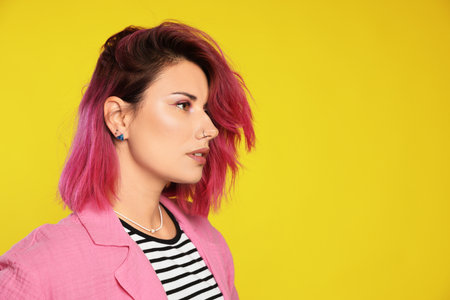 Beautiful woman with pink dyed hair on yellow background, space for textの写真素材