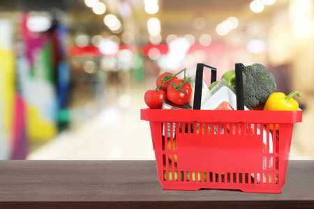 Red shopping basket full of groceries on wooden table in supermarket. Space for textの写真素材
