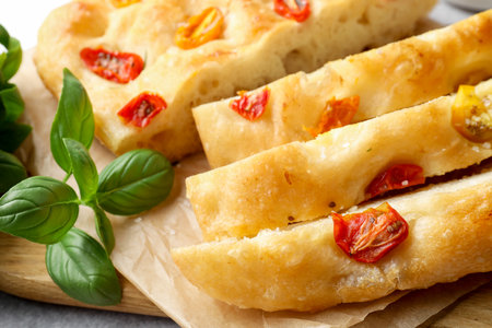Cut delicious focaccia with tomatoes and basil on table, closeupの写真素材