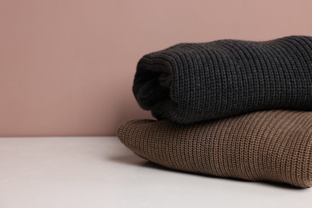 Stack of woolen sweaters on white table against color background, closeup. Space for text