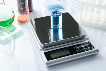 Scale with beaker of sample and other laboratory equipment on white background, closeupの写真素材