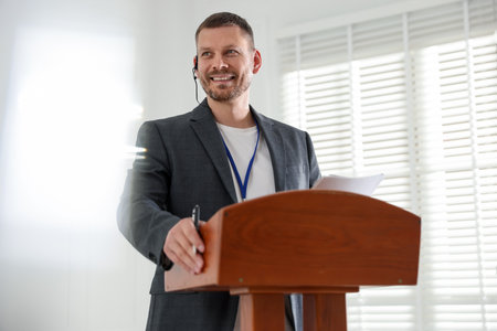 Man giving public speech with microphone at lectern indoorsの写真素材