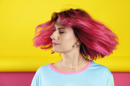 Beautiful woman with pink dyed hair shaking head on color backgroundの写真素材