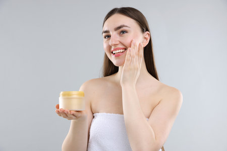 Smiling woman applying collagen cream on grey backgroundの写真素材