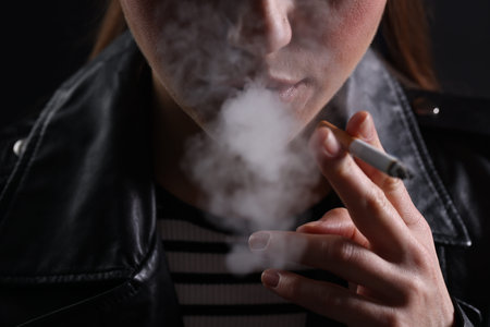 Woman smoking cigarette on black background, closeup