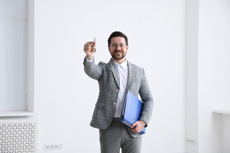 Real estate agent holding key with house shaped keychain and folder indoors