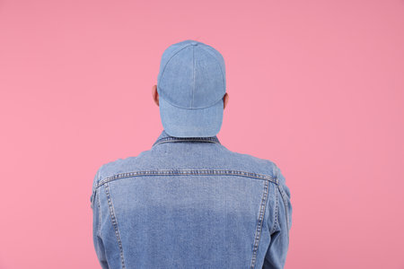 Young man wearing stylish denim baseball hat on pink backgroundの写真素材
