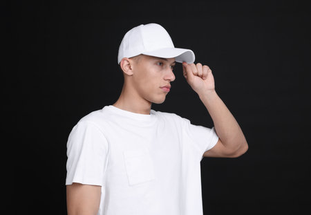 Young man wearing stylish white baseball hat on black backgroundの写真素材