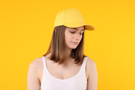 Young woman wearing stylish baseball hat on yellow backgroundの写真素材