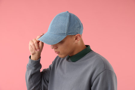 Young man in stylish baseball hat on pink backgroundの写真素材