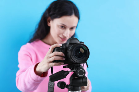 Woman with professional video camera on light blue background, selective focus. Space for textの写真素材