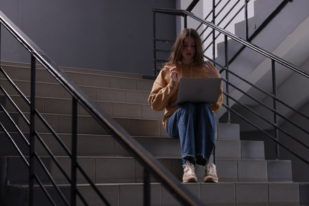 Cyber bullying. Upset teenage girl with laptop on stairs indoors. Space for textの写真素材