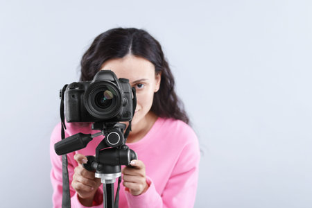 Woman with professional video camera on light gray background, selective focus. Space for text