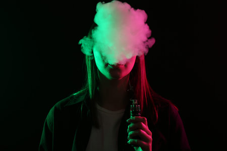 Woman using electronic smoking device in neon lights on black background