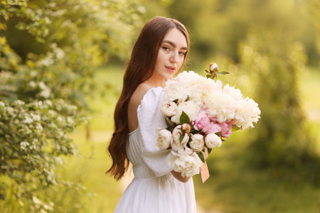 Beautiful woman with bouquet of peonies in parkの写真素材