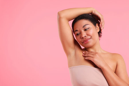Woman showing hairless armpit after epilation procedure on pink background, space for text
