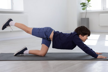 Cute boy practicing yoga on mat indoors