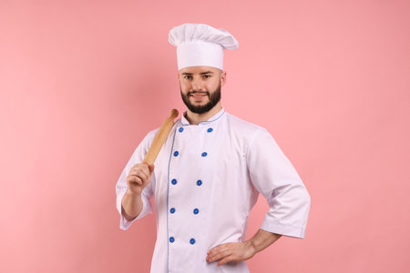 Happy confectioner in uniform holding rolling pin on pink backgroundの写真素材