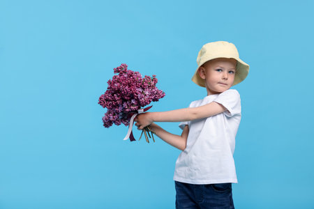 Little boy with bouquet of lilac flowers on light blue backgroundの写真素材