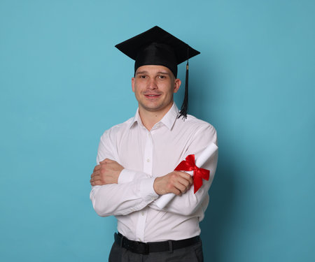 Happy student with diploma after graduation on light blue backgroundの写真素材