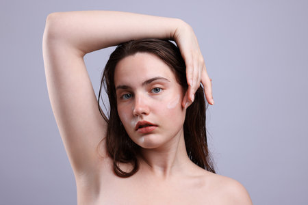 Portrait of woman with skincare product on her face against grey background, closeupの写真素材