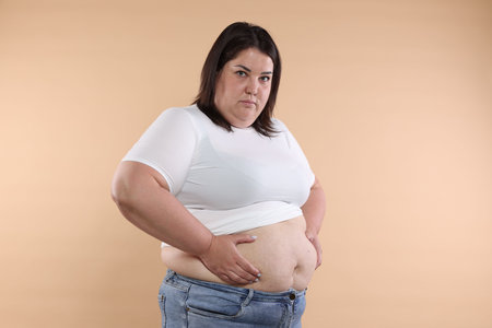 Woman with excessive belly fat on beige backgroundの写真素材
