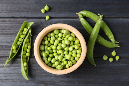 Fresh ripe green peas on black wooden table, flat lay