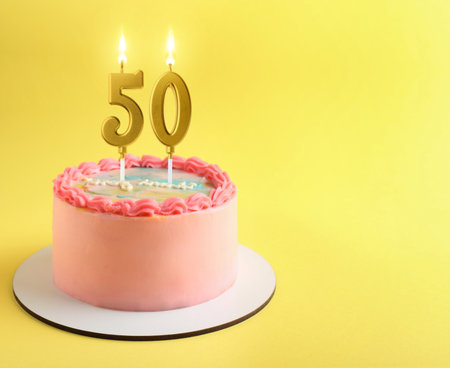Yummy cake with burning number shaped candles on yellow background, space for text. 50th birthday or other special occasionの写真素材