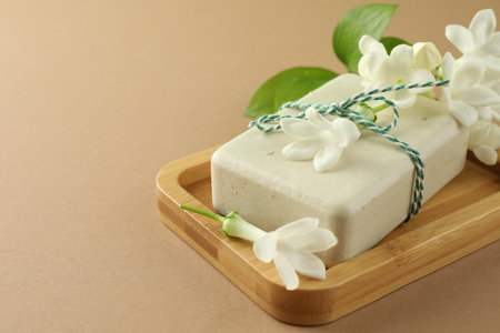 Bar of soap and jasmine flowers on light brown background, closeup. Space for textの写真素材