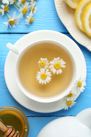 Delicious chamomile tea in cup, fresh flowers, lemon and honey on light blue wooden table, flat layの写真素材