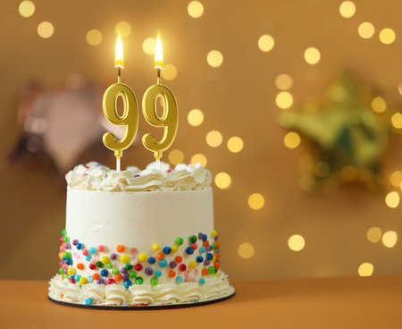 Yummy cake with burning number shaped candles against blurred lights, space for text. 99th birthday...