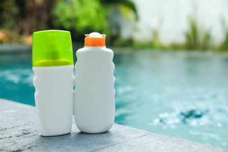 Bottles of sun protection products on stone surface near swimming pool outdoors, space for text