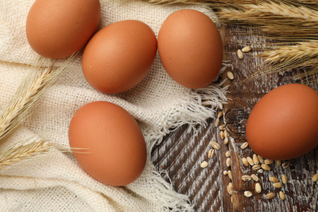 Raw eggs, fabric and spikes of wheat on wooden table, flat layの写真素材