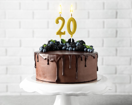 Yummy chocolate cake with berries and burning number shaped candles on table. 20th birthday or other special occasionの写真素材