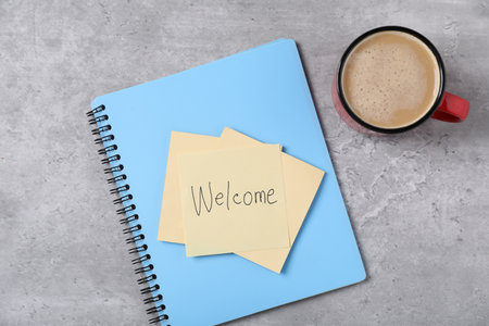 Sticky note with word Welcome, notebook and coffee on grey table, flat layの写真素材